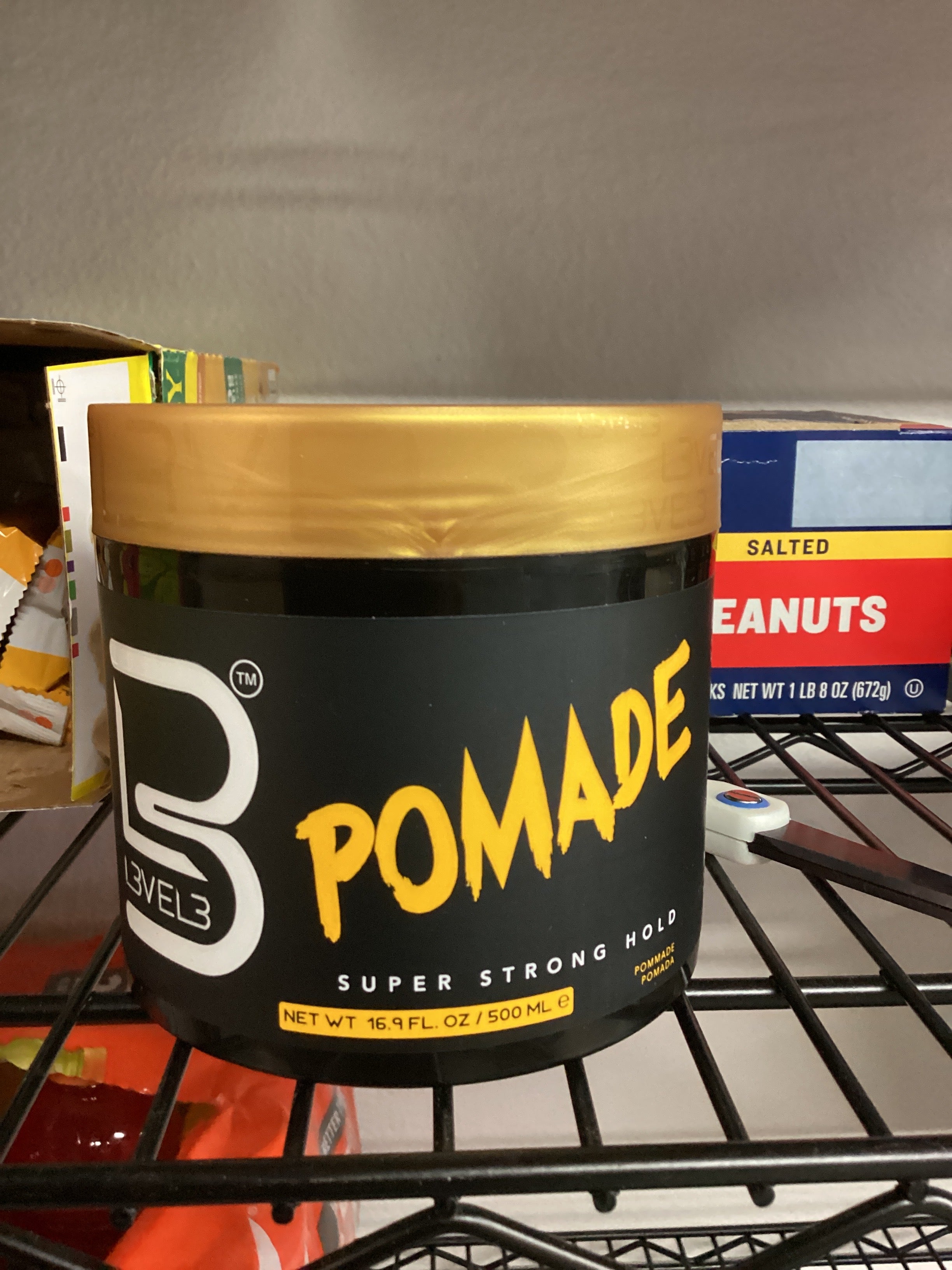 Black and gold container of pomade on a shelf with other products